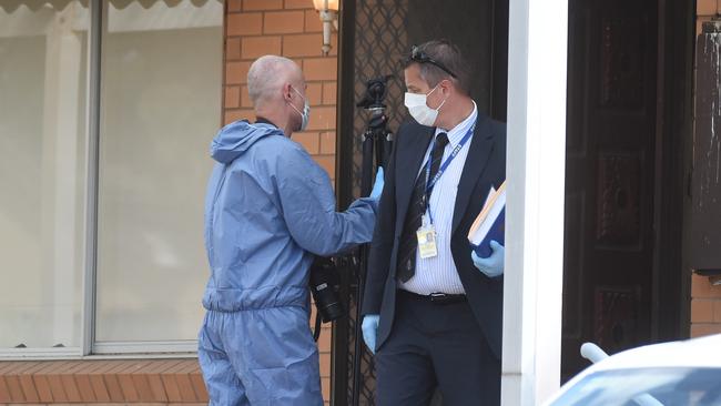 A detective and a forensics officer talk on the veranda of the house