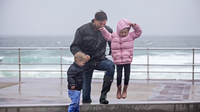 Anton Murry with his children Franklin and Margeaux jumping in puddles as they leave Bondi Beach. Picture: Adam Yip