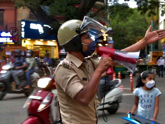 A police officer uses a loud speaker to warn and disperse people gathered in a commercial area in Bangalore on July 14, 2020, as residents prepare for a week-long lockdown to contain the surge of COVID-19 coronavirus cases. (Photo by Manjunath Kiran / AFP)