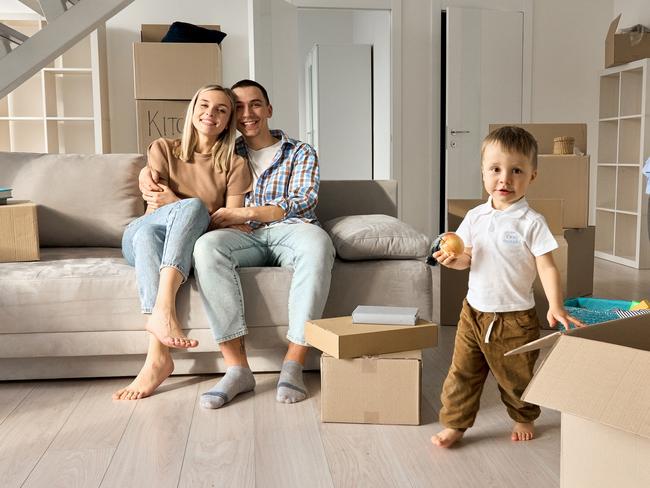 Happy family new home owners with child son in living room on moving day. Young couple apartment buyers relaxing on couch with kid boy playing around boxes. Relocation and house renovation, removal.