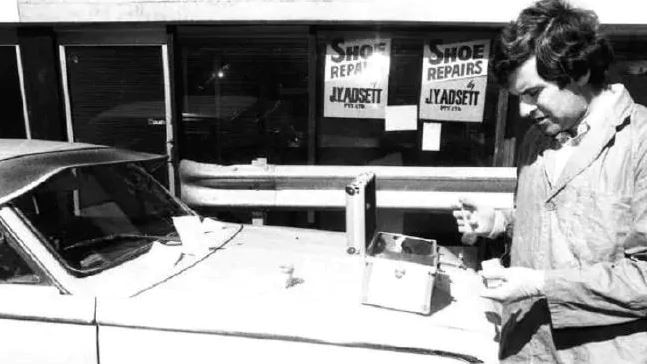 Senior Constable L. Jones examines a vehicle parked behind the Lennons Plaza Hotel on Burnett Lane. He's dusting for fingerprints.