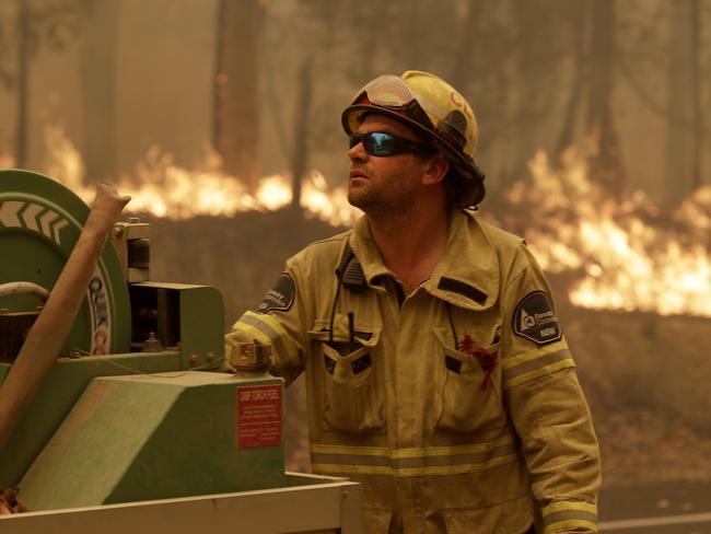 A Forest Corporation worker manages a fire hose as he battles a fire near Moruya, Australia, Saturday, Jan. 4, 2020. Australia's Prime Minister Scott Morrison called up about 3,000 reservists as the threat of wildfires escalated Saturday in at least three states with two more deaths, and strong winds and high temperatures were forecast to bring flames to populated areas including the suburbs of Sydney. (AP Photo/Rick Rycroft)