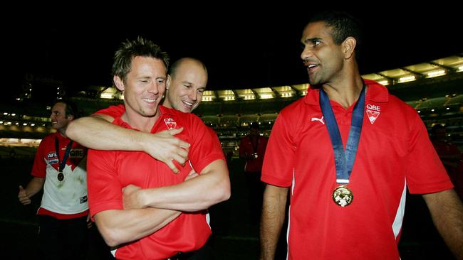 New Adelaide coach Matthew Nicks hugs Stuart Maxfield after both missed Sydney’s 2005 grand final win as teammate Michael O'Loughlin looks on with his premiership medal.