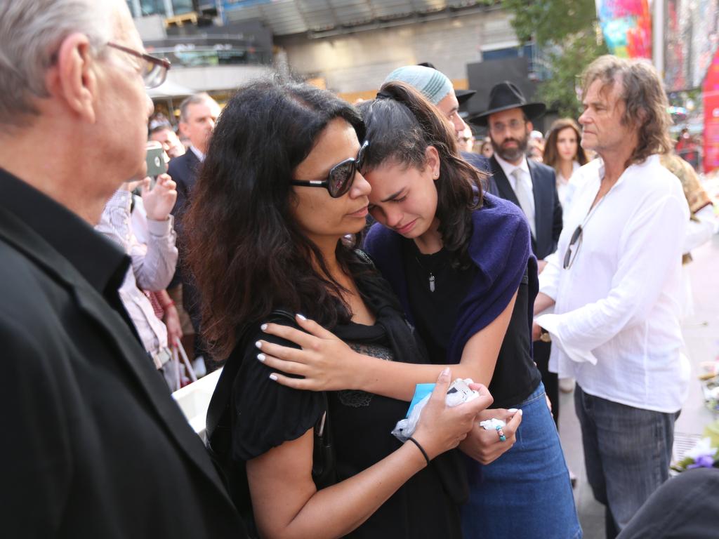 18. After the siege came the tears. Tori Johnson’s father, artist Ken Johnson, (far right) sought some solace from the outpouring of a city as a sea of flowers covered Martin Place in the days after the tragedy.Tori’s youngest sister Rada is seen as she breaks down during the ceremony. Picture: Rohan Kelly