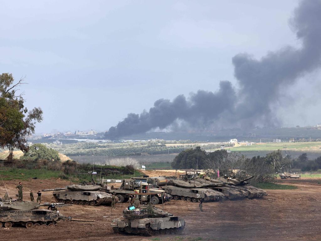 Israeli soldiers stand next to tanks at a position in Israel near the border with the Gaza Strip as smoke billows over the Gaza Strip after Israeli bombardment on January 14. Picture: Menahem Kahana / AFP