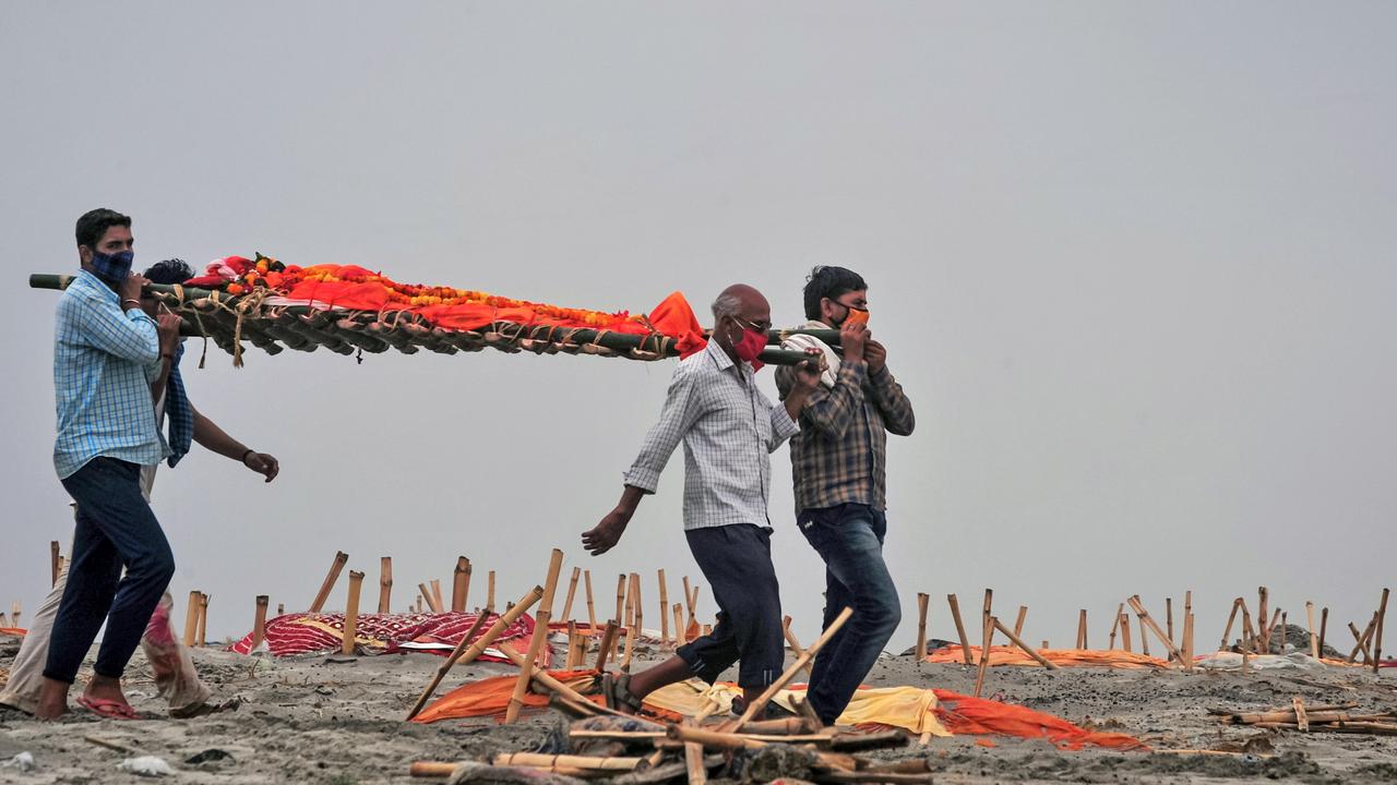 Relatives in Uttar Pradesh state carry a relative’s body through partly-exposed sand graves on the Ganges River. Picture: Ritesh Shukla/Getty Images