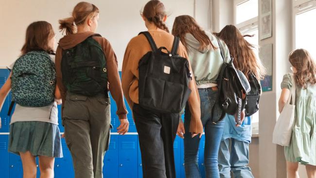 Back view of six female high school students walking in school corridor against blue lockers during break.High School students, Generic, Picture: Getty Images