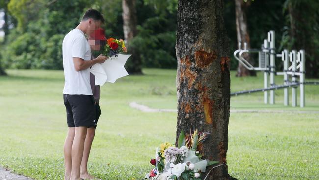 A man and a boy lay floral tributes at the scene of a fatal crash at Manoora, where an allegedly stolen Toyota Yaris left Pease St near the Saltwater Creek bridge and struck a tree. Bradley Smith, 14, died at the scene, and five other children aged 12 to 15 were taken to Cairns Hospital with injuries. Picture: Brendan Radke