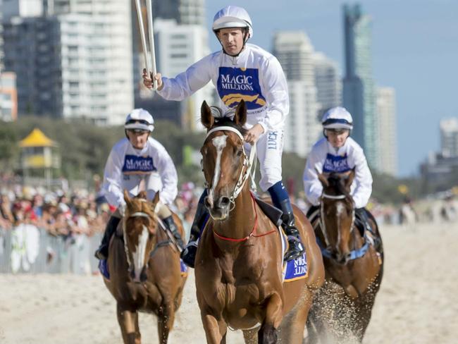 Champion jockey Hugh Bowman holds the Queens baton aloft  as he rides along Surfers Paradise beach 4at the Magic Millions Barrier draw in Surfers Paradise this morning. Pic Tim Marsden