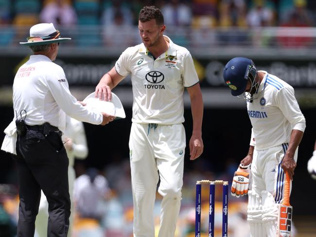 Australia's bowler Josh Hazlewood takes his hat back from the umpire after his over on day four of the third cricket Test match between Australia and India at The Gabba in Brisbane on December 17, 2024. (Photo by David GRAY / AFP) / âIMAGE RESTRICTED TO EDITORIAL USE - STRICTLY NO COMMERCIAL USE --