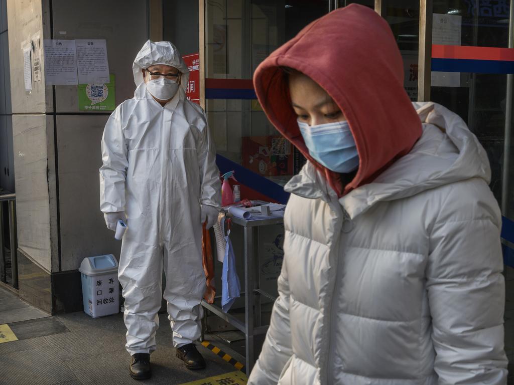 A Chinese worker wears a protective suit and mask as he waits to check the temperature of customers entering a grocery store. Picture: Kevin Frayer/Getty Images.