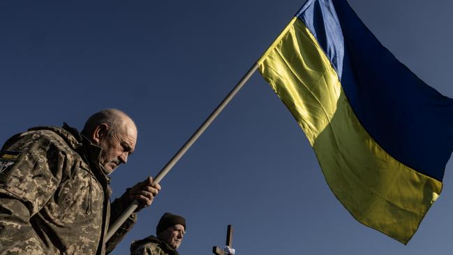 FASTIV, UKRAINE - FEBRUARY 24: A soldier holds a flag during the joint military funerals for Volodymyr Semenyuk, 43, and his military comrade Serhiy Voytenko, 53, on February 24, 2025 in Fastiv, Ukraine. Both soldiers were with the 47th brigade, killed together on February 18th in Kursk (Russia) when a glide bomb hit their position. Monday marks three years since Russia launched a full-scale invasion of Ukraine, with Russian forces continuing to make slow but steady gains across Ukraine's eastern front, while Ukrainian forces have staged a counter-offensive into Russian territory. The milestone comes as tensions between Ukraine and its key ally, the United States, have been escalating since  Ukraine was excluded last week from bilateral talks between American and Russian diplomats, on laying the groundwork for peace negotiations. (Photo by Paula Bronstein/Getty Images)