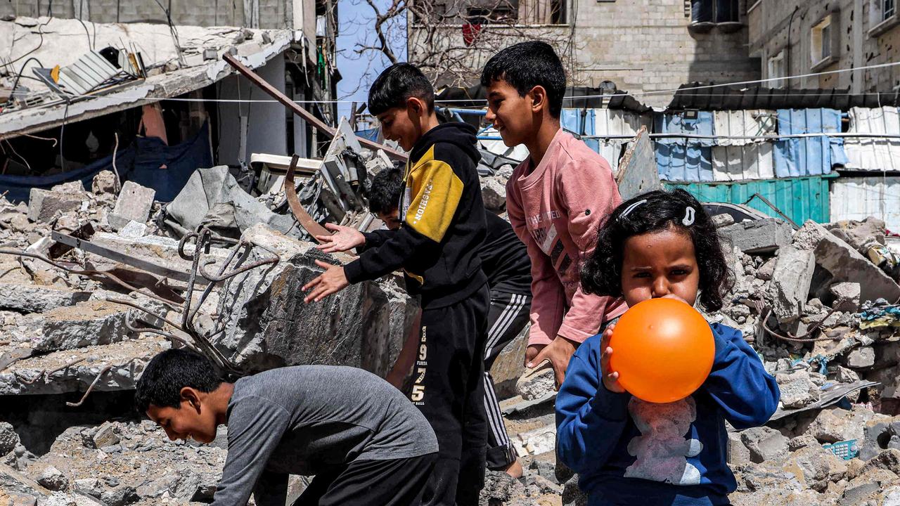 A girl blows a balloon as behind her boys search through the rubble of a destroyed building in Rafah in the southern Gaza Strip. Picture: AFP