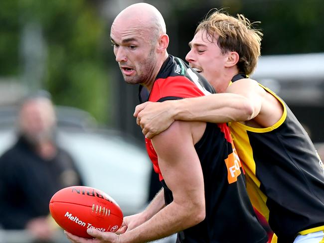 Joshua Grabham of Riddell handballs whilst being tackled during the round two RDFNL Bendigo Bank Seniors match between Riddell and Kyneton at Riddells Creek Recreation Reserve, on April 13,2024, in Diggers Rest, Australia. (Photo by Josh Chadwick)