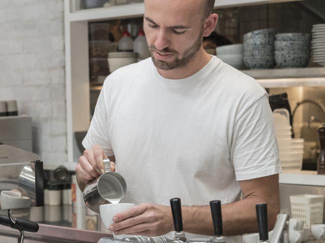 Customer and barista at cool hip coffee shop bar while proprietor makes a cappucino with frothy milk