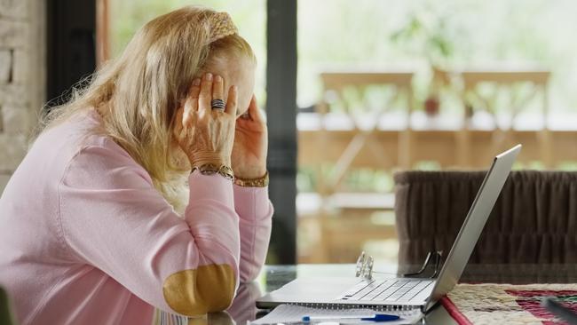 Side view of senior woman suffering a stress headache while working on home budget using laptop; Mortgage home loan money stress generic