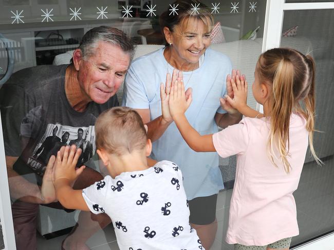 Grandparents Wayne and Lynn Smith get a visit from the grandkids Montana 6 (pink shirt), Isaiah 4 (white shirt), and Zac Ayoub 2 (grey shirt) at their home in Woolooware. Following advice to stay isolated from Covid-19 they only do the visit through the glass door. Picture Rohan Kelly.