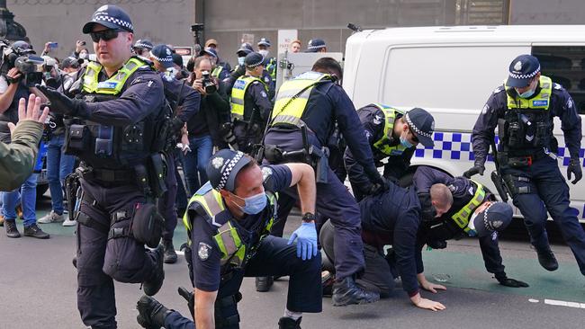 Police officers detain a man as protesters gather outside Parliament House in Melbourne,