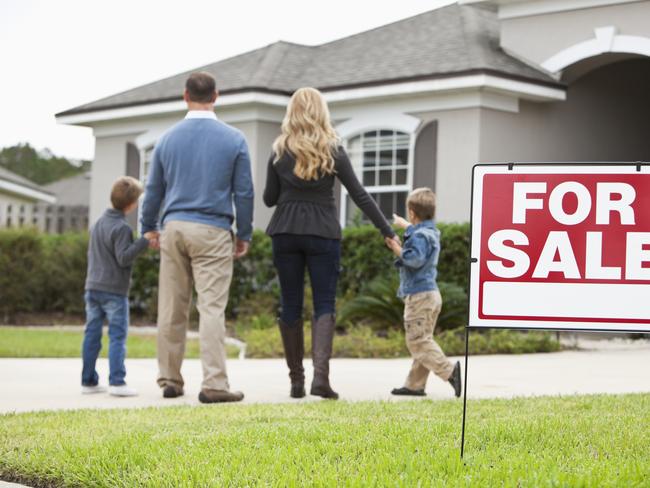 Family with two boys (4 and 6 years) standing in front of house with FOR SALE sign in front yard.  Focus on sign.