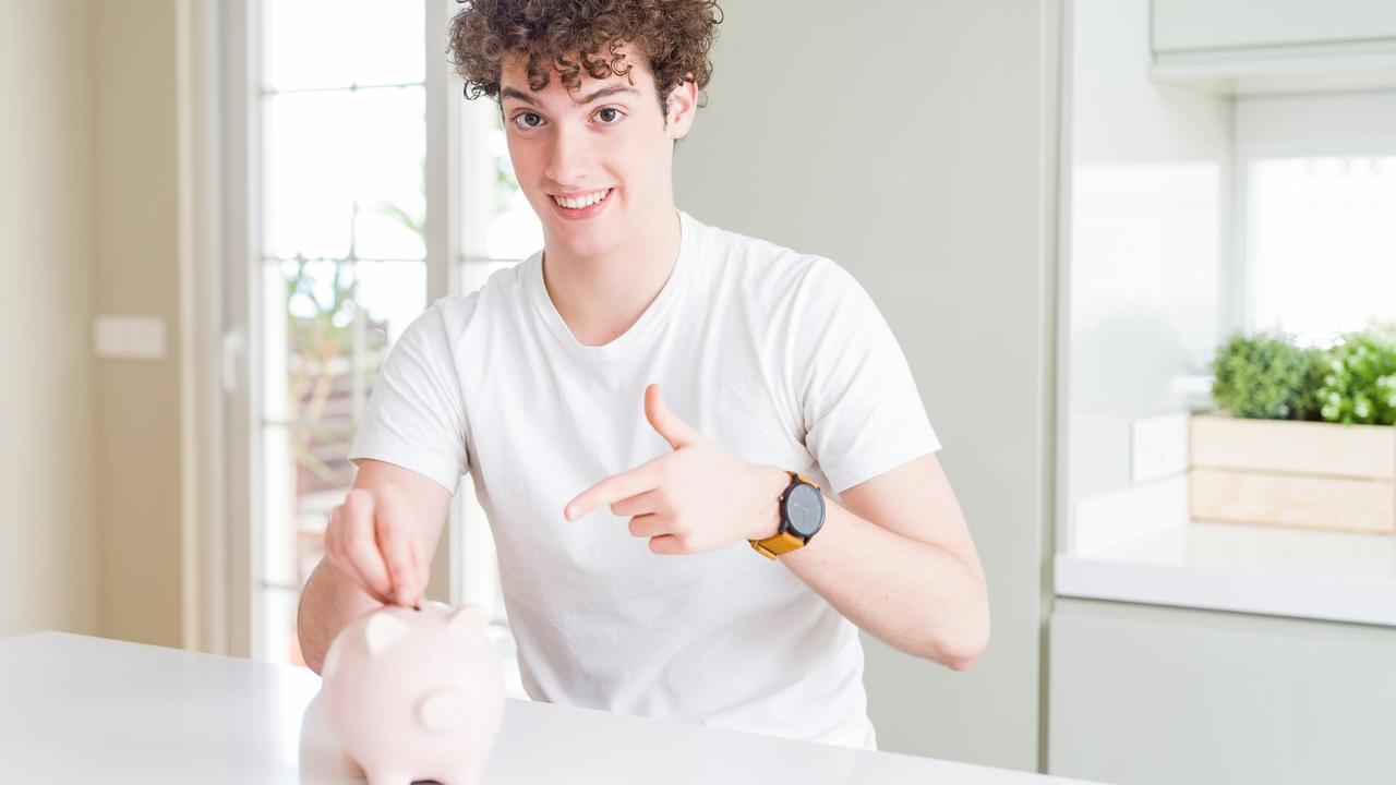 Young man investing money using piggy bank at home very happy pointing with hand and finger