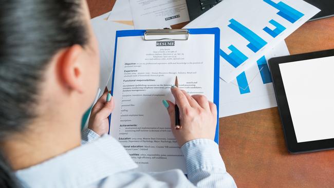 CAREERS: Young businesswoman or recruiter reviewing resume for opening position, sitting at the desk with laptop and documents in office