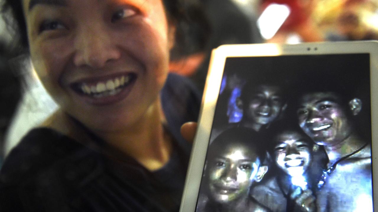 Thanaporn Promthep displays an image of her son Duangpetch, nicknamed ‘Dom’ (with light), and soccer coach Ekapol Chantawong (right), after hearing the news the group had been found. Picture: AFP Photo / Lillian Suwanrumpha