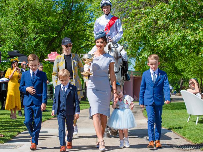 Melbourne Cup Tour ambassadors Kerrin and Cathy McEvoy — carrying the 1919 Melbourne Cup — with their children at The Park, Flemington, on October 28. Picture: Jason Edwards