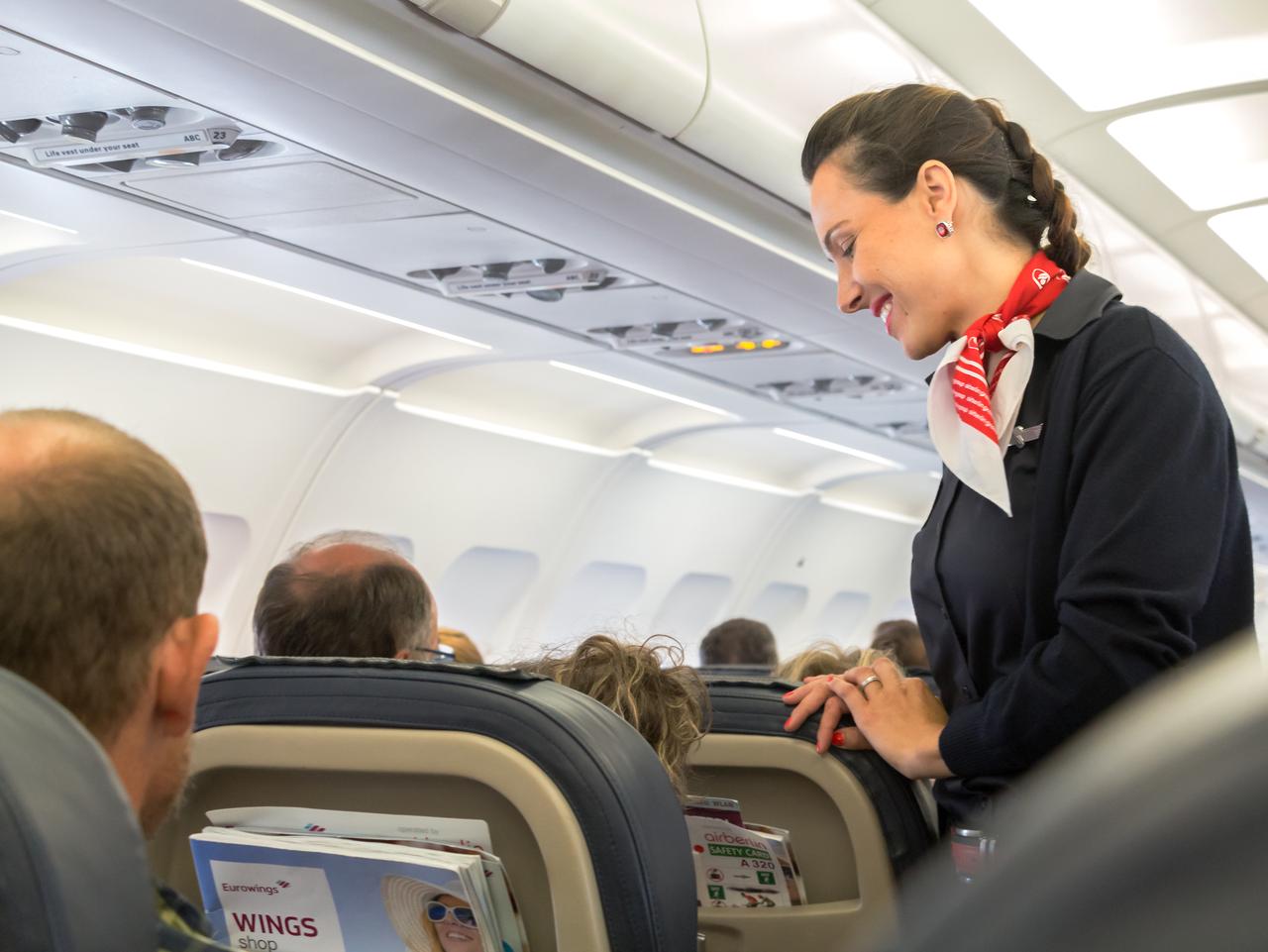 Thessaloniky: A female flight attendant is speaking with a passenger sitting in the economy class of the route Thessaloniky - Munich of Eurowings Airline.