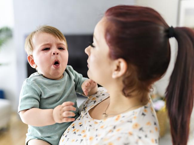 A mother holding child baby on the living room. The baby is sick having some cough. Istock Photo