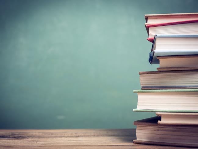 Back to school. Textbooks stacked on wooden school desk in front of green chalkboard. Classroom setting.