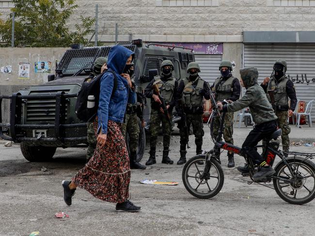 A Palestinian woman and a child riding a bicycle pass in front of members of the security forces in the Balata camp, near the occupied West Bank city of Nablus, on December 15, 2020. - In Palestinian refugee camps in the Israeli-occupied West Bank some residents are taking up arms for a potential power struggle when president Mahmud Abbas, 85, finally leaves the stage. Abbas, leader of the dominant Fatah movement and of the Palestinian Authority (PA), has promised elections in 2021, for the first time in almost 15 years. (Photo by JAAFAR ASHTIYEH / AFP)