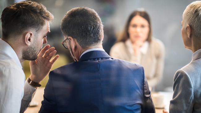 Male member of human resource team whispering to his colleague during a job interview in the office. The view is through glass.