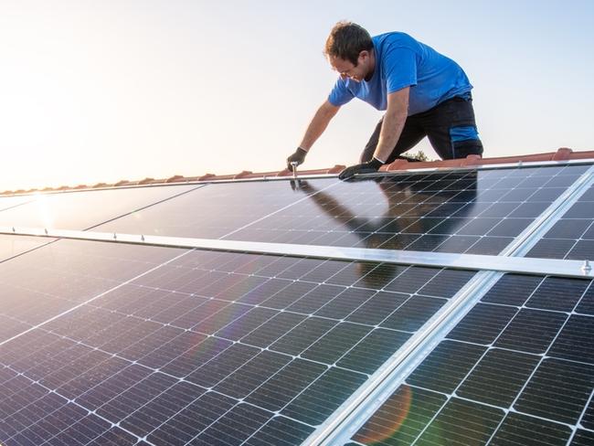 kneeling professional fixing solar panels from the top of a house roof, side view of the roof with sun reflection