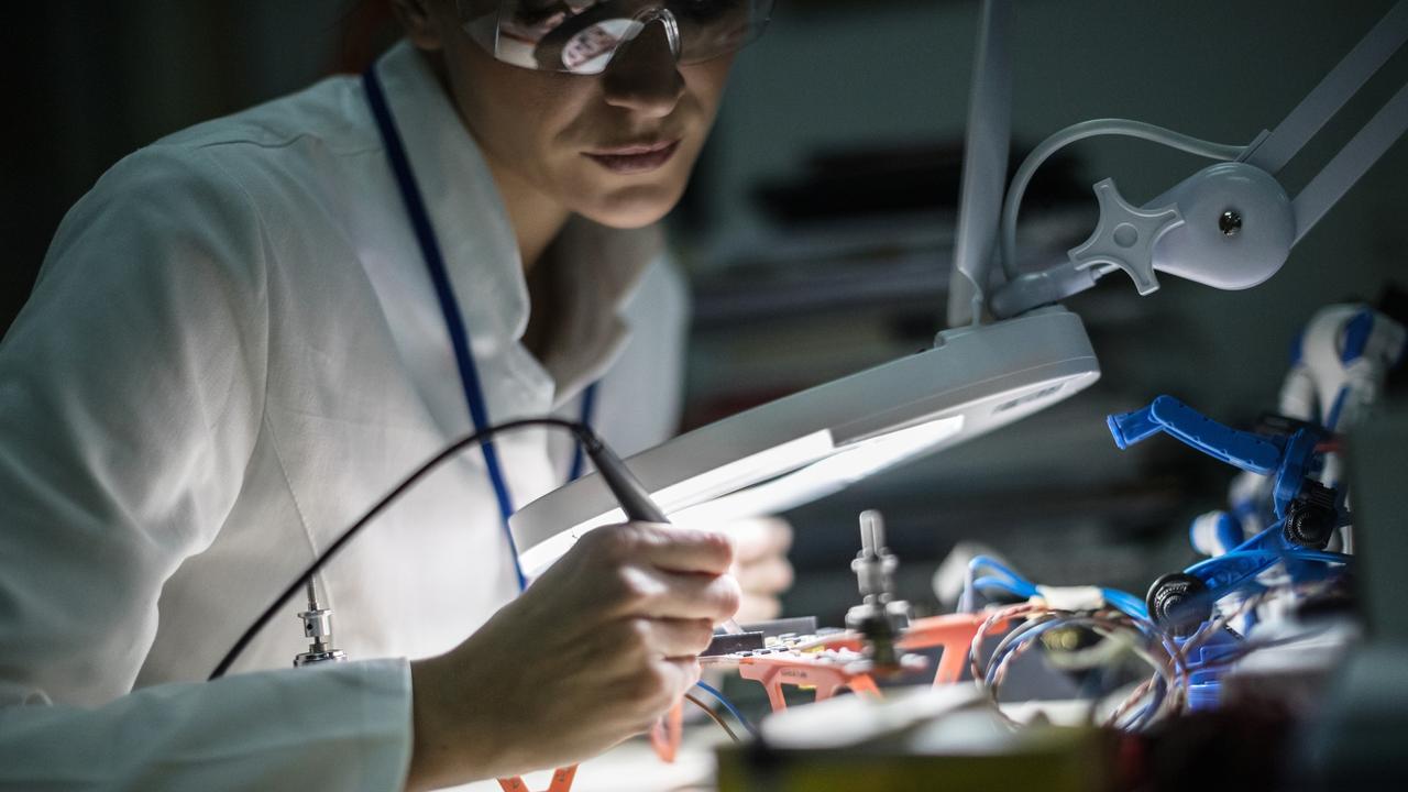 ELECTRONIC/ ENGINEERING CAREERS FOR WOMEN:  Mid adult female electrician working on drone at desk in industry, using magnifying glass;  Robotics generic