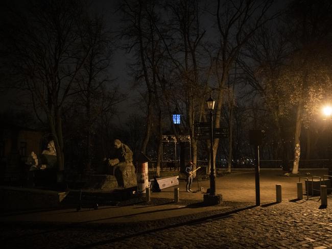 A busker plays a guitar near a street light as the city is showed in darkness in Kyiv, Ukraine. Electricity and heating outages across Ukraine caused by missile and drone strikes to energy infrastructure. Picture: Getty Images