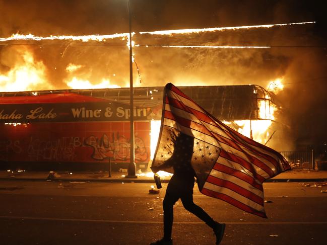 A protester carries a U.S. flag upside down, a sign of distress, next to a burning building in Minneapolis. Picture: AP