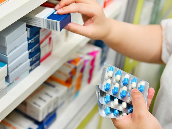 Pharmacist holding medicine box and capsule pack in pharmacy drugstore.