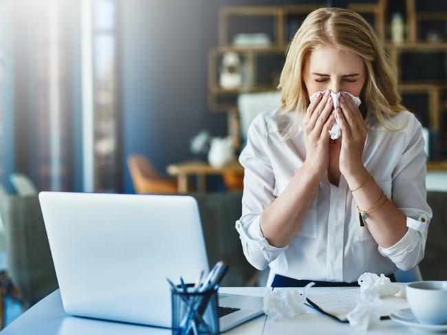 Shot of a businesswoman using a tissue to sneeze in while being seated in the office, flu season. Picture: Istock