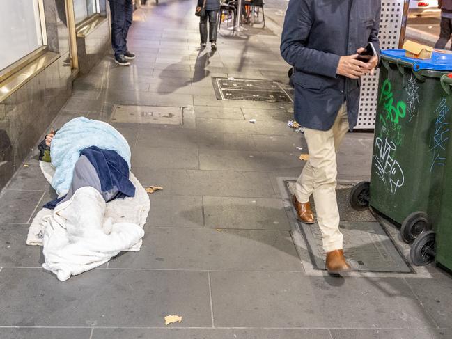 Pedestrians step past a person asleep on Russell St. Picture: Jake Nowakowski