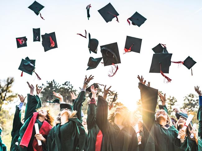 Generic stock photo showing a large group of happy college students celebrating their graduation day outdoors while throwing their caps up in the air.