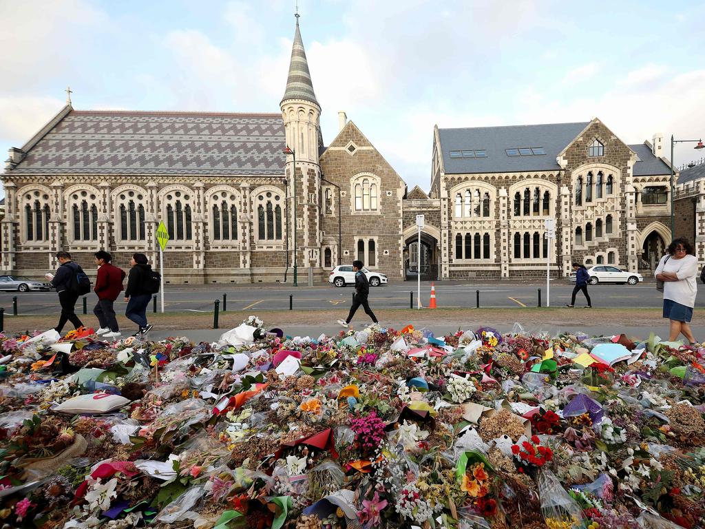 People walk past flowers and tributes displayed in memory of the twin mosque massacre victims outside the Botanical Gardens in Christchurch. Picture: AFP