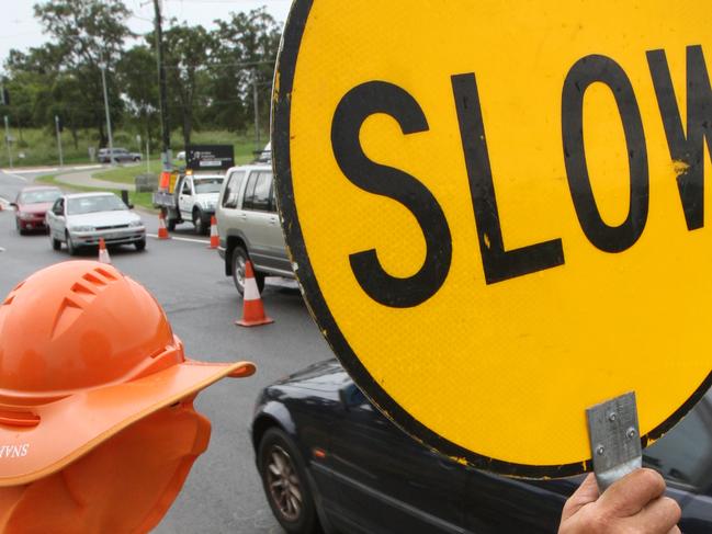 Traffic controller with 'Slow' sign at roadworks.