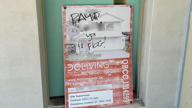 A tradie leaves a sign that reads “pay up ya flog” on a site belonging to collapsed builder DC Living, which went under earlier this month.