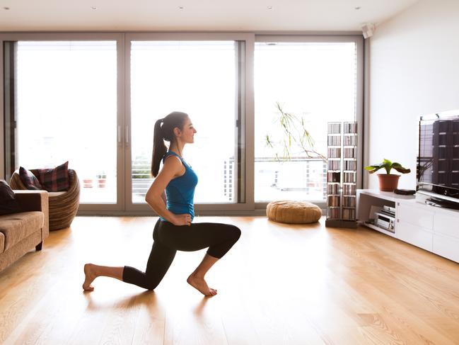 Beautiful young woman working out at home in living room, doing yoga or pilates exercise, stretching legs.