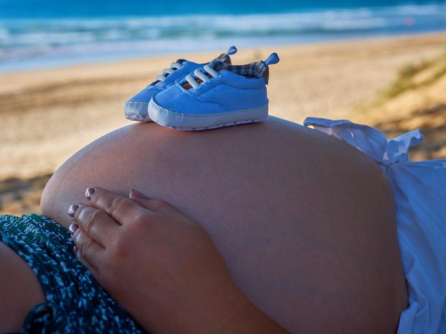 Maternity sunrise showing belly abdomen with baby birth due soon. Sunrise pregnancy waves ocean and sandy shorefront at dawn.