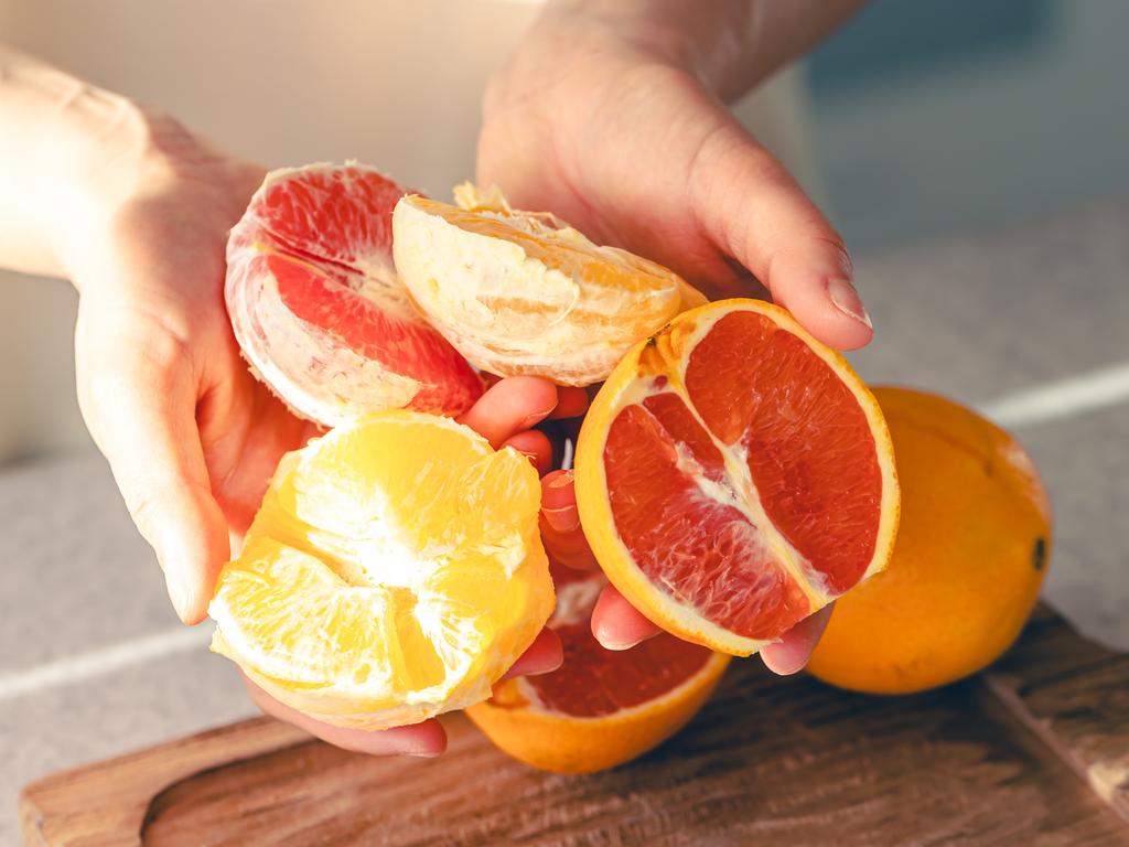 Peeled oranges in female hands and on a wooden cutting board for juice. The process of making orange juice in the home kitchen.