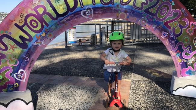 Leo Switchik-Reardon, 2, of Manly, rides his scooter under the WorldPride 2023 Rainbow Arch next to Manly Wharf, created by artist Skye Burton. Picture: Jim O'Rourke