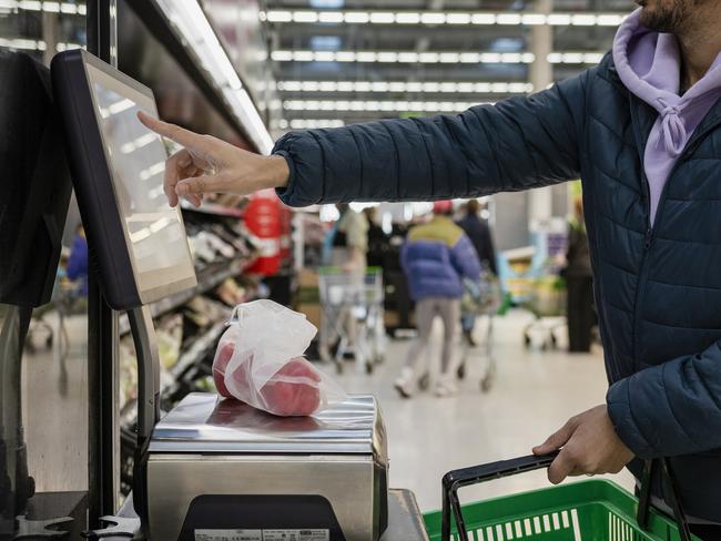 Side view of a man shopping in a supermarket while on a budget. He is weighing the items at the self service checkout in the North East of England. The peppers are in a sustainable mesh bag.