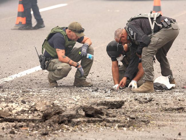 Members of Israeli security forces inspect the impact site of a reported rocket fired from Lebanon, on the Horeshim interchange in central Israel on October 1, 2024. Air raid sirens sounded in central Israel on October 1 and an AFP journalist heard explosions in the city of Tel Aviv, with the military saying projectiles had been fired from Lebanon. Police said one projectile hit a road near the central town of Kfar Kassen, wounding a man who was struck by shrapnel and treated by emergency services. (Photo by Jack GUEZ / AFP)