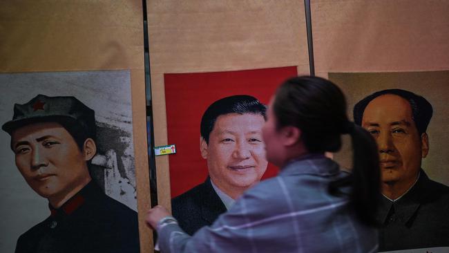 A vendor hangs a portrait of the Chinese President Xi Jinping next to pictures of the former Chinese leader Mao Zedong. Picture: AFP